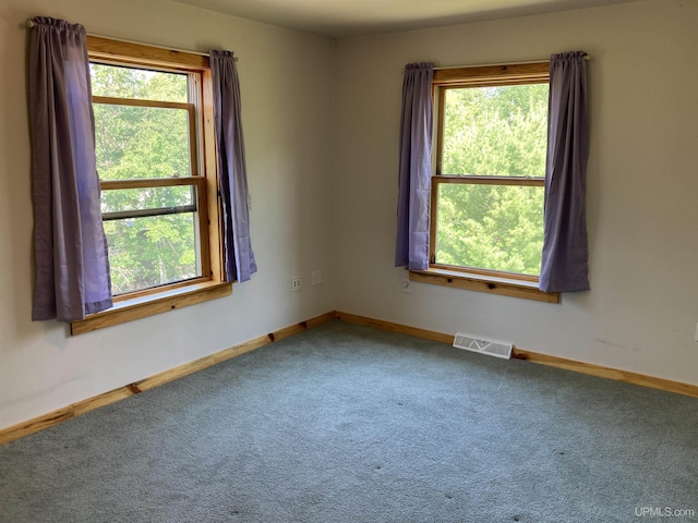 carpeted spare room featuring plenty of natural light, visible vents, and baseboards