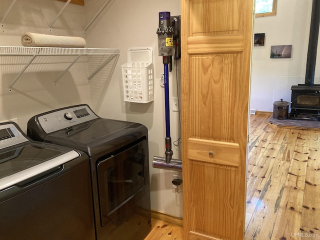 laundry room featuring washing machine and clothes dryer, light wood-style flooring, a wood stove, laundry area, and baseboards