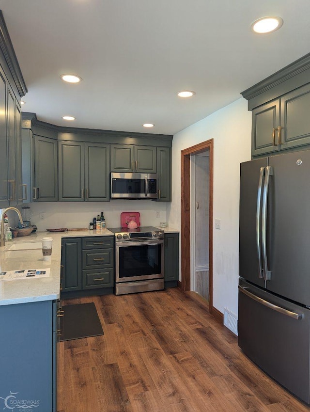 kitchen with appliances with stainless steel finishes, light stone counters, dark wood-type flooring, and sink