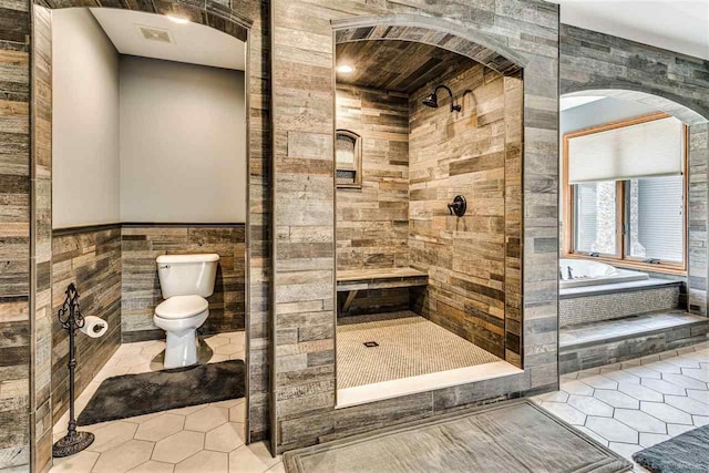 full bathroom with toilet, a stall shower, tile walls, and tile patterned floors