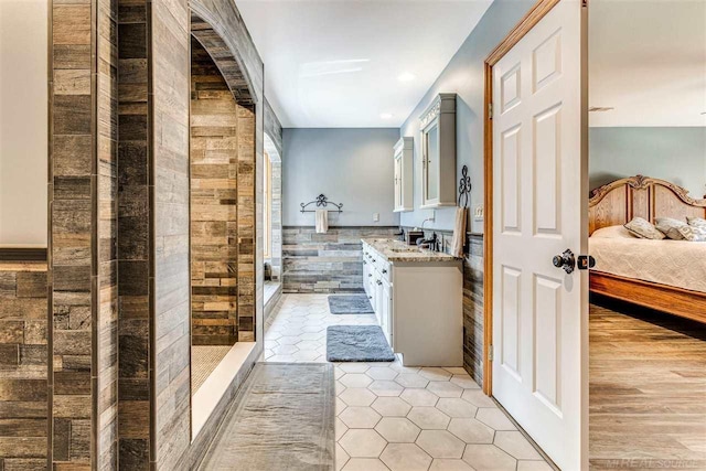 ensuite bathroom featuring a walk in shower, tile patterned flooring, connected bathroom, vanity, and tile walls