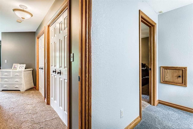 hallway featuring carpet, baseboards, and a textured wall