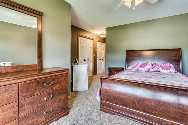 unfurnished bedroom featuring light carpet, two closets, and ceiling fan