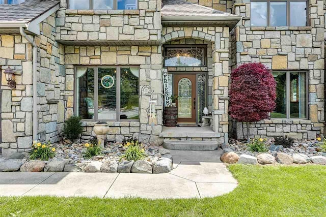 view of exterior entry with stone siding and a shingled roof