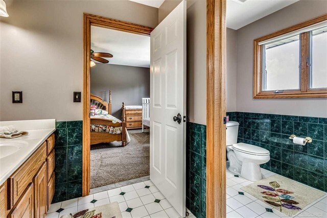 bathroom featuring tile patterned flooring, toilet, vanity, ceiling fan, and tile walls