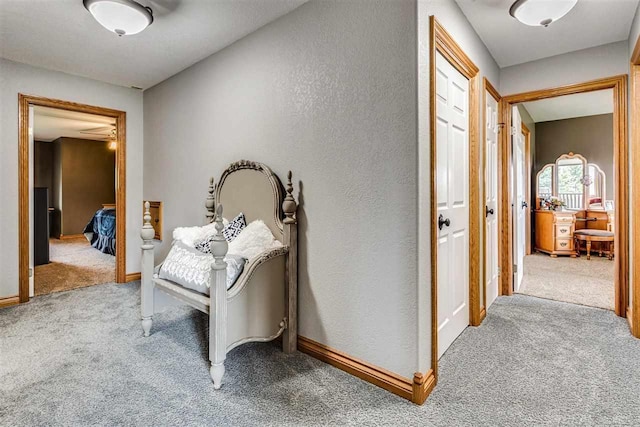 hallway with baseboards, a textured wall, and light colored carpet