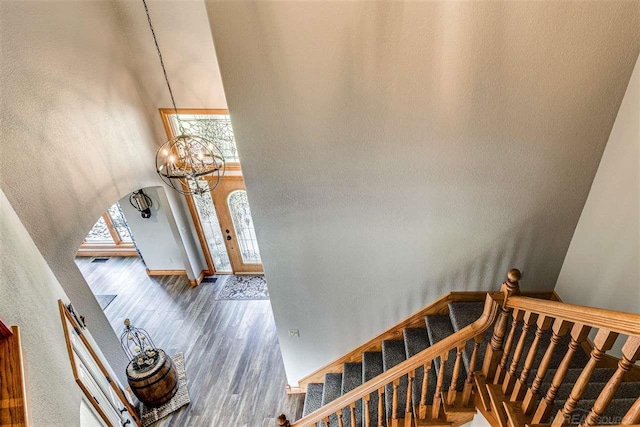 stairs with arched walkways, wood finished floors, a towering ceiling, and a chandelier