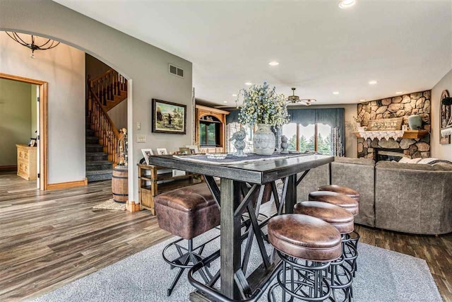 dining room with stairs, a stone fireplace, dark wood-style flooring, and visible vents