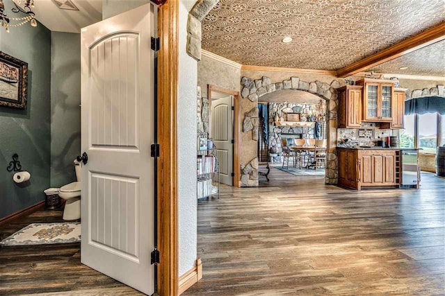 kitchen featuring arched walkways, dark wood-type flooring, glass insert cabinets, and crown molding