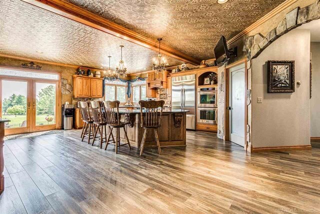 kitchen featuring ornamental molding, appliances with stainless steel finishes, an inviting chandelier, and wood-type flooring