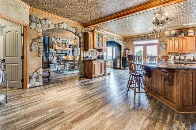 kitchen with a breakfast bar area, tasteful backsplash, a notable chandelier, wood-type flooring, and ornamental molding