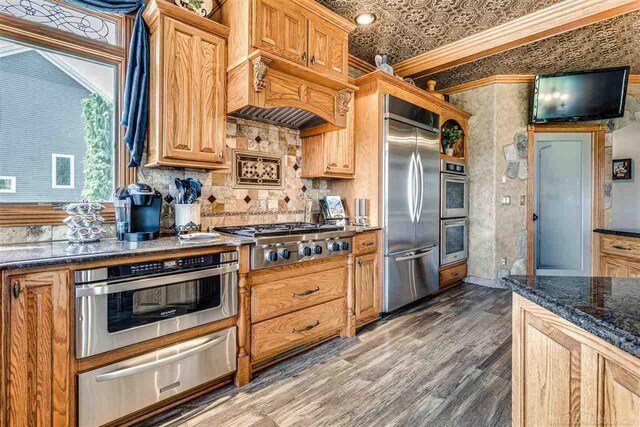 kitchen with crown molding, tasteful backsplash, dark stone counters, stainless steel appliances, and wood-type flooring