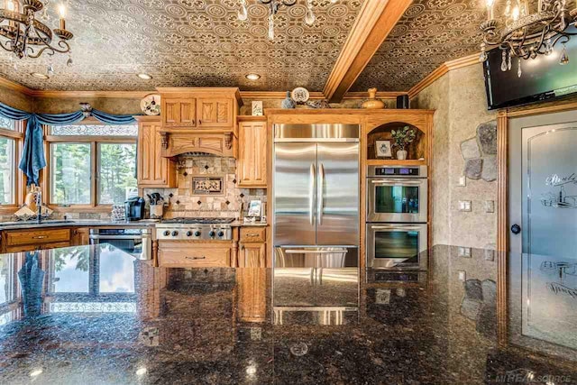 kitchen with dark stone counters, ornamental molding, sink, custom range hood, and appliances with stainless steel finishes