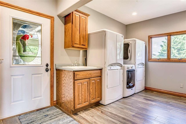 laundry room featuring stacked washer / dryer, a sink, baseboards, light wood-type flooring, and cabinet space