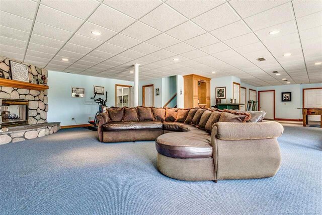 living room with a drop ceiling, carpet floors, and a stone fireplace