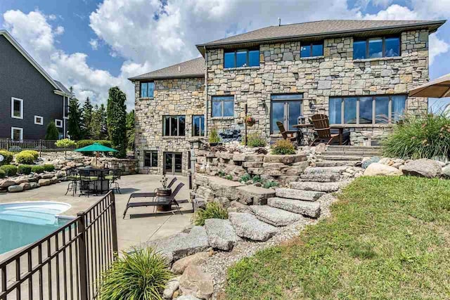 back of house featuring stone siding, a patio area, and fence