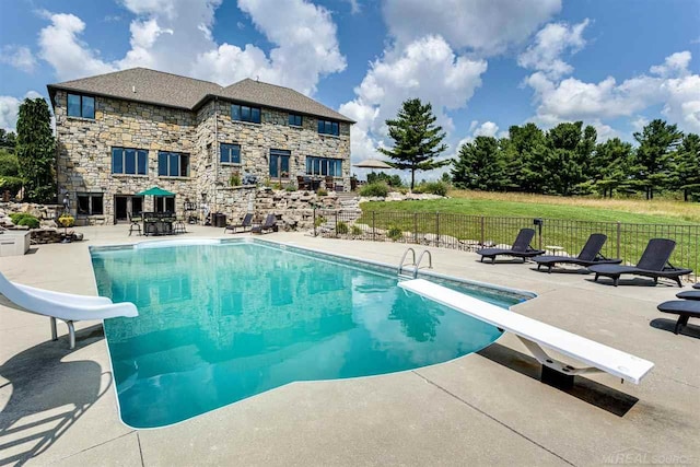 view of swimming pool with a water slide, a patio, and a diving board