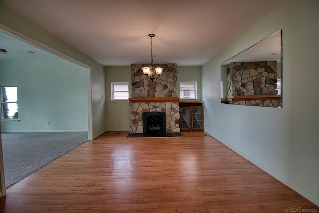 unfurnished living room featuring hardwood / wood-style flooring, a stone fireplace, and an inviting chandelier