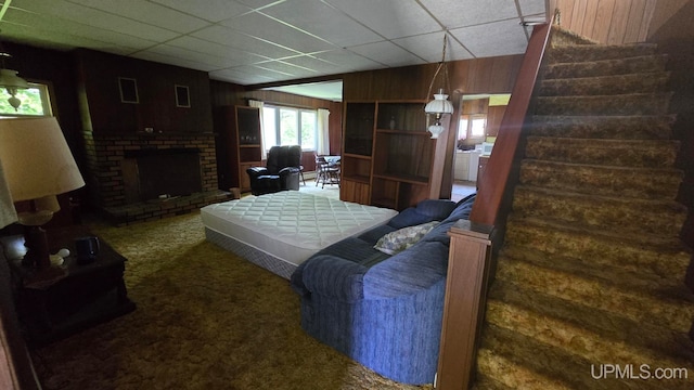 carpeted living room featuring a fireplace, a drop ceiling, and wooden walls