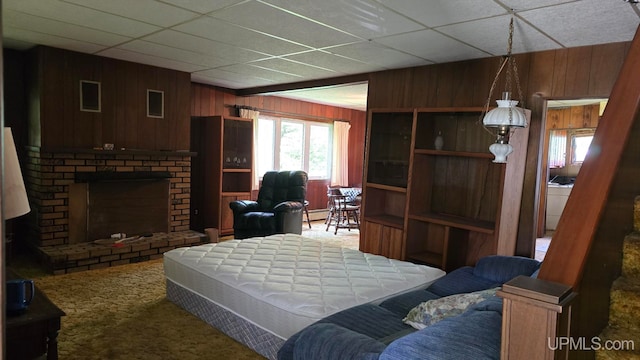 bedroom with a drop ceiling, carpet, a brick fireplace, and wooden walls