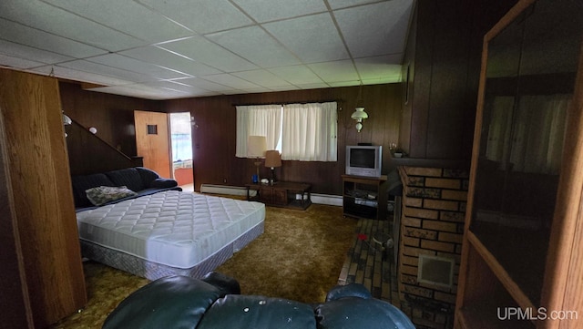 carpeted bedroom featuring wooden walls, a drop ceiling, and baseboard heating