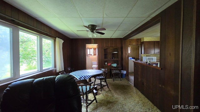 living room featuring a drop ceiling, wooden walls, and ceiling fan