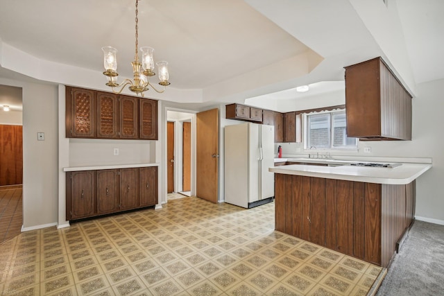 kitchen featuring an inviting chandelier, sink, kitchen peninsula, white fridge, and dark brown cabinetry