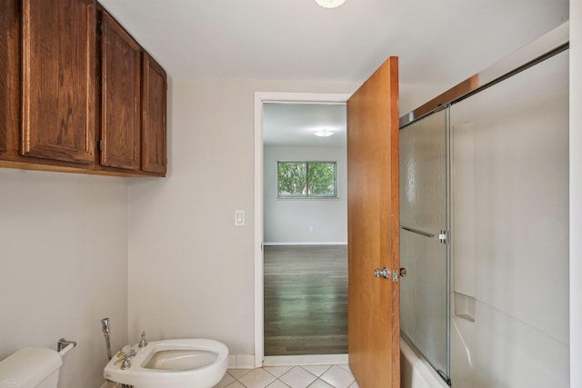 bathroom with tile patterned flooring, toilet, bath / shower combo with glass door, and a bidet