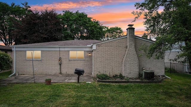 property exterior at dusk featuring a lawn, central AC, and a patio area