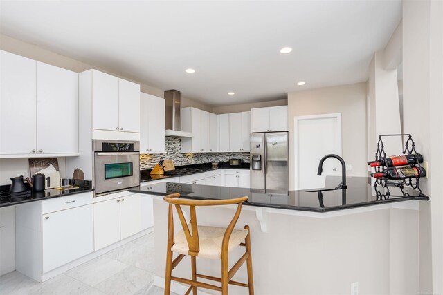 kitchen with light tile patterned flooring, tasteful backsplash, wall chimney range hood, white cabinets, and appliances with stainless steel finishes