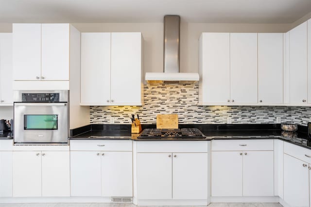 kitchen with black gas cooktop, oven, white cabinetry, wall chimney range hood, and decorative backsplash