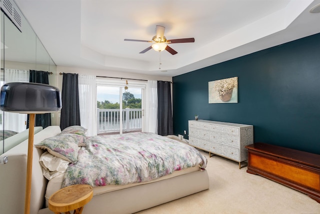 carpeted bedroom featuring access to exterior, a tray ceiling, visible vents, and a ceiling fan