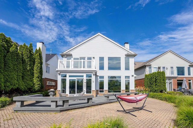 back of property with a balcony, a patio area, and a chimney