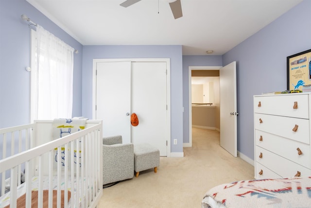 bedroom featuring light carpet, a crib, baseboards, a ceiling fan, and a closet