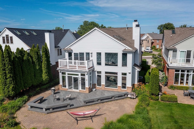 back of house featuring a balcony, a chimney, a residential view, a wooden deck, and brick siding