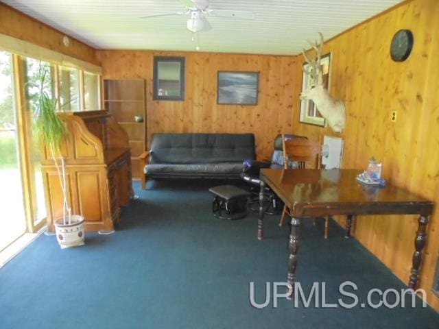 carpeted office space with ceiling fan and wood walls