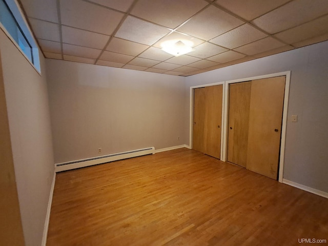 unfurnished bedroom with multiple closets, wood-type flooring, a baseboard heating unit, and a drop ceiling