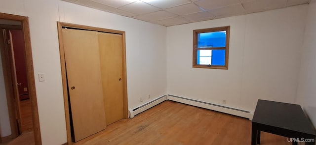 unfurnished bedroom with a closet, a drop ceiling, baseboard heating, and light hardwood / wood-style flooring