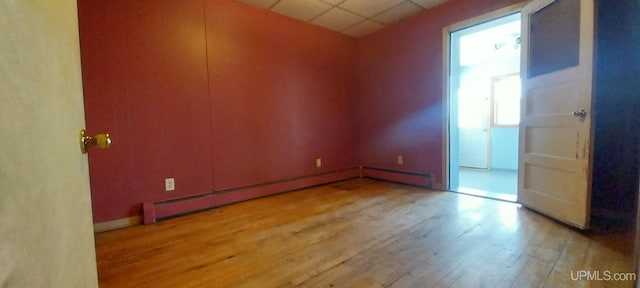 empty room with a baseboard radiator, a paneled ceiling, and light wood-type flooring