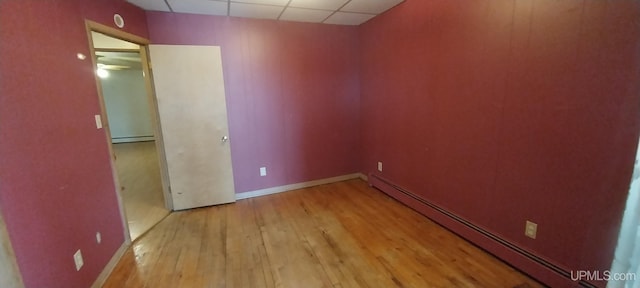 unfurnished room with a drop ceiling, light hardwood / wood-style flooring, and a baseboard heating unit