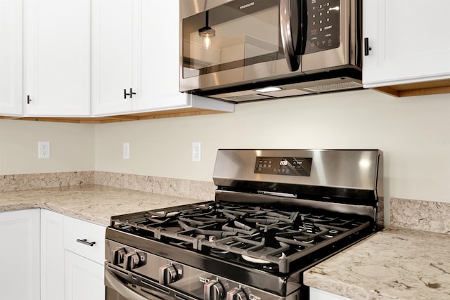 kitchen with light stone counters, hanging light fixtures, stainless steel appliances, and white cabinets