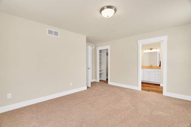 unfurnished bedroom with light colored carpet, ensuite bath, a closet, and a walk in closet