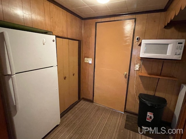 kitchen with white appliances, wooden walls, and dark colored carpet