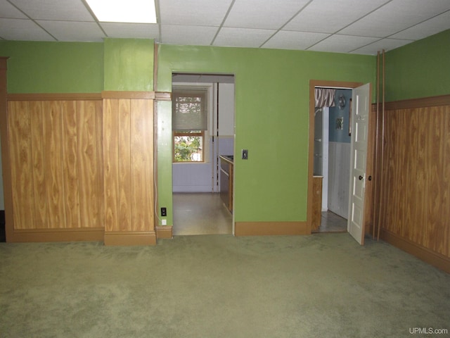 carpeted empty room featuring a paneled ceiling, a wainscoted wall, and wooden walls