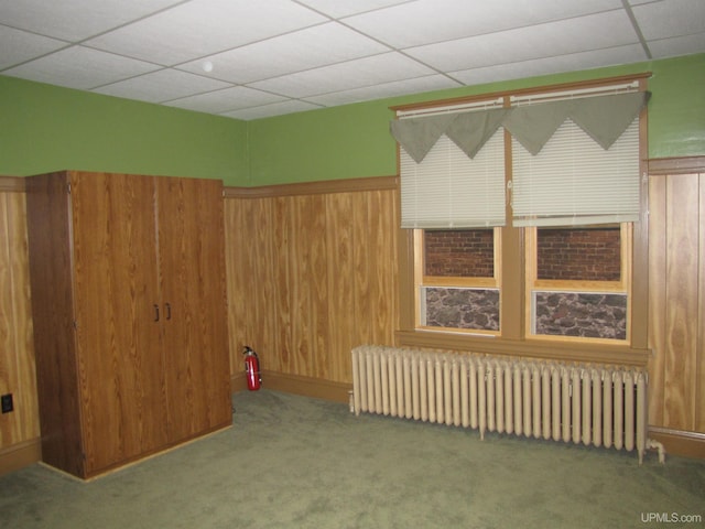 carpeted spare room featuring radiator, a drop ceiling, and wooden walls