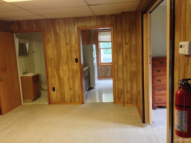 hallway featuring light carpet, wooden walls, a drop ceiling, and a sink