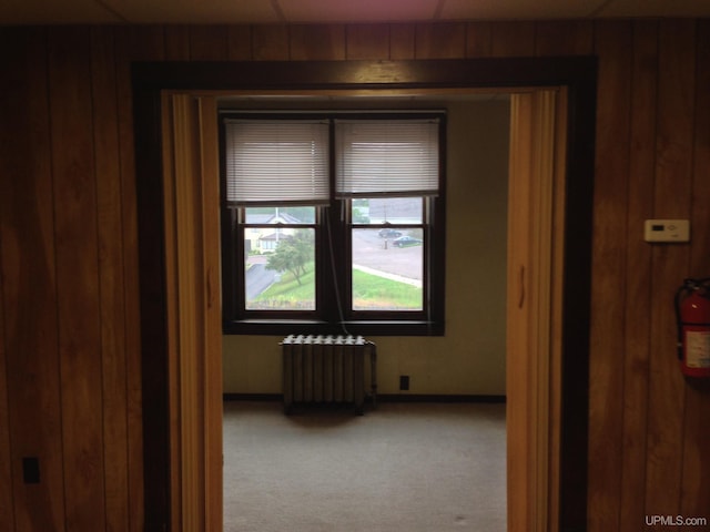 carpeted spare room with wood walls, radiator heating unit, and baseboards