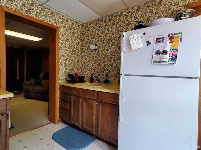 kitchen featuring freestanding refrigerator, light countertops, a sink, and wallpapered walls