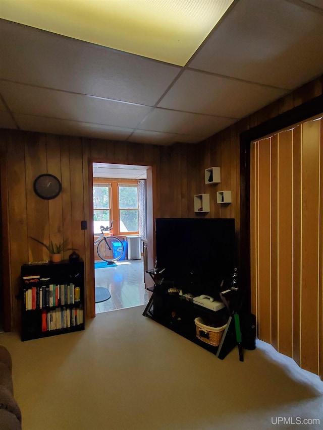 living area featuring a paneled ceiling and wooden walls