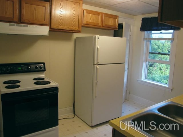 kitchen featuring under cabinet range hood, freestanding refrigerator, brown cabinets, electric range oven, and light floors